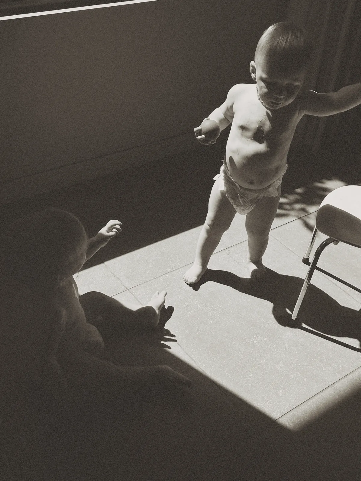 A baby walking through a hard wedge of afternoon sun, long shadow across the floor