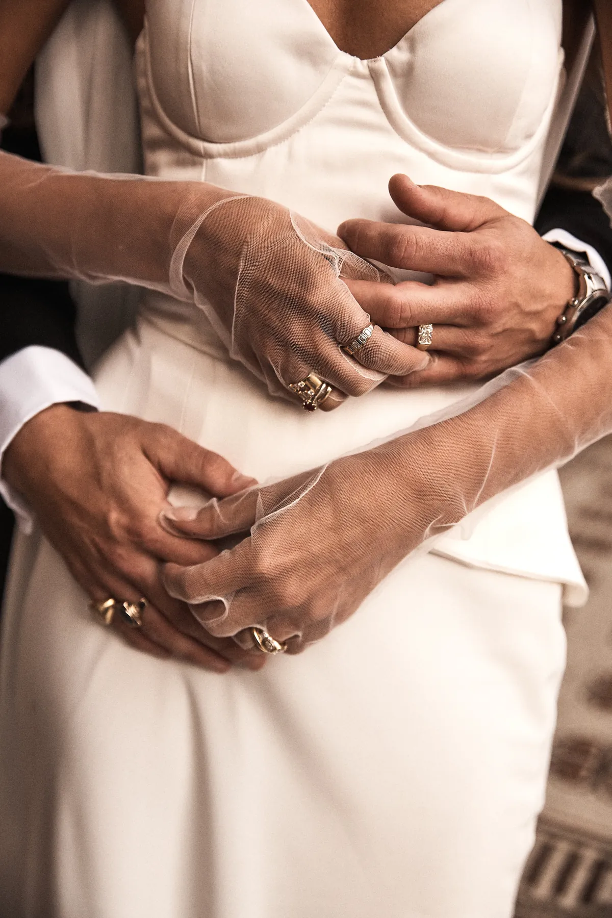 Close detail of the groom's hands around the bride's waist, sheer gloves and rings