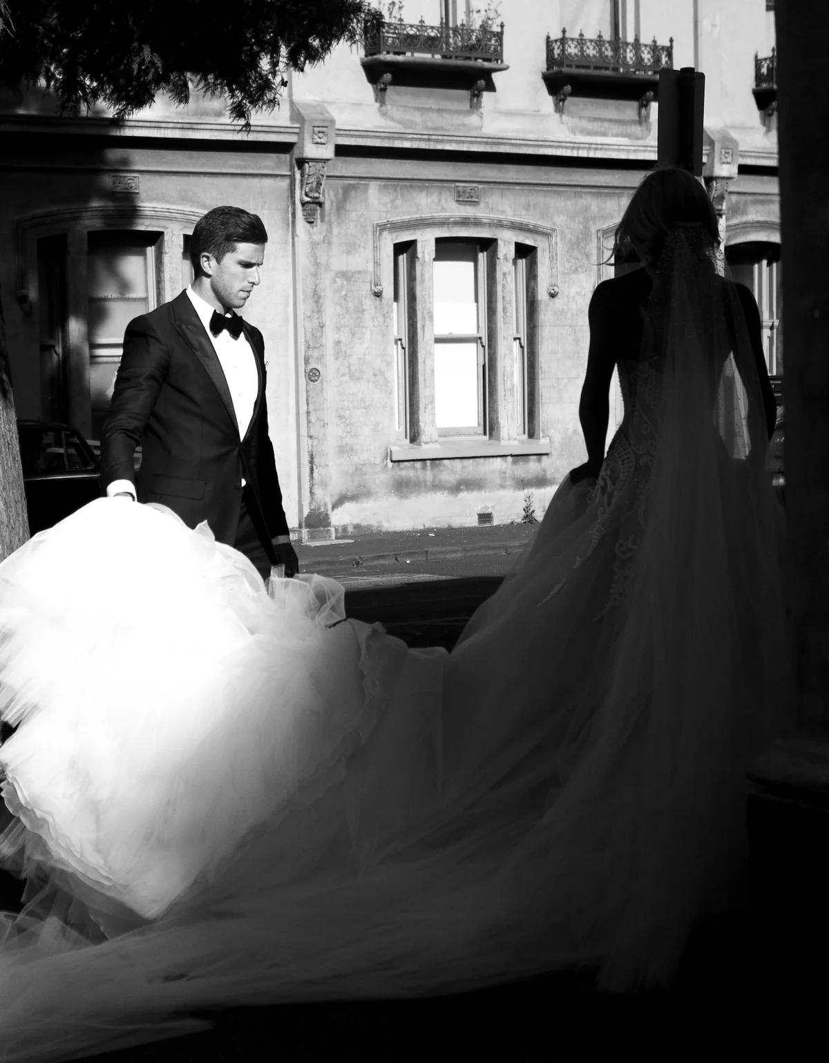 Groom carrying the bride's train along a Melbourne terrace street — black and white