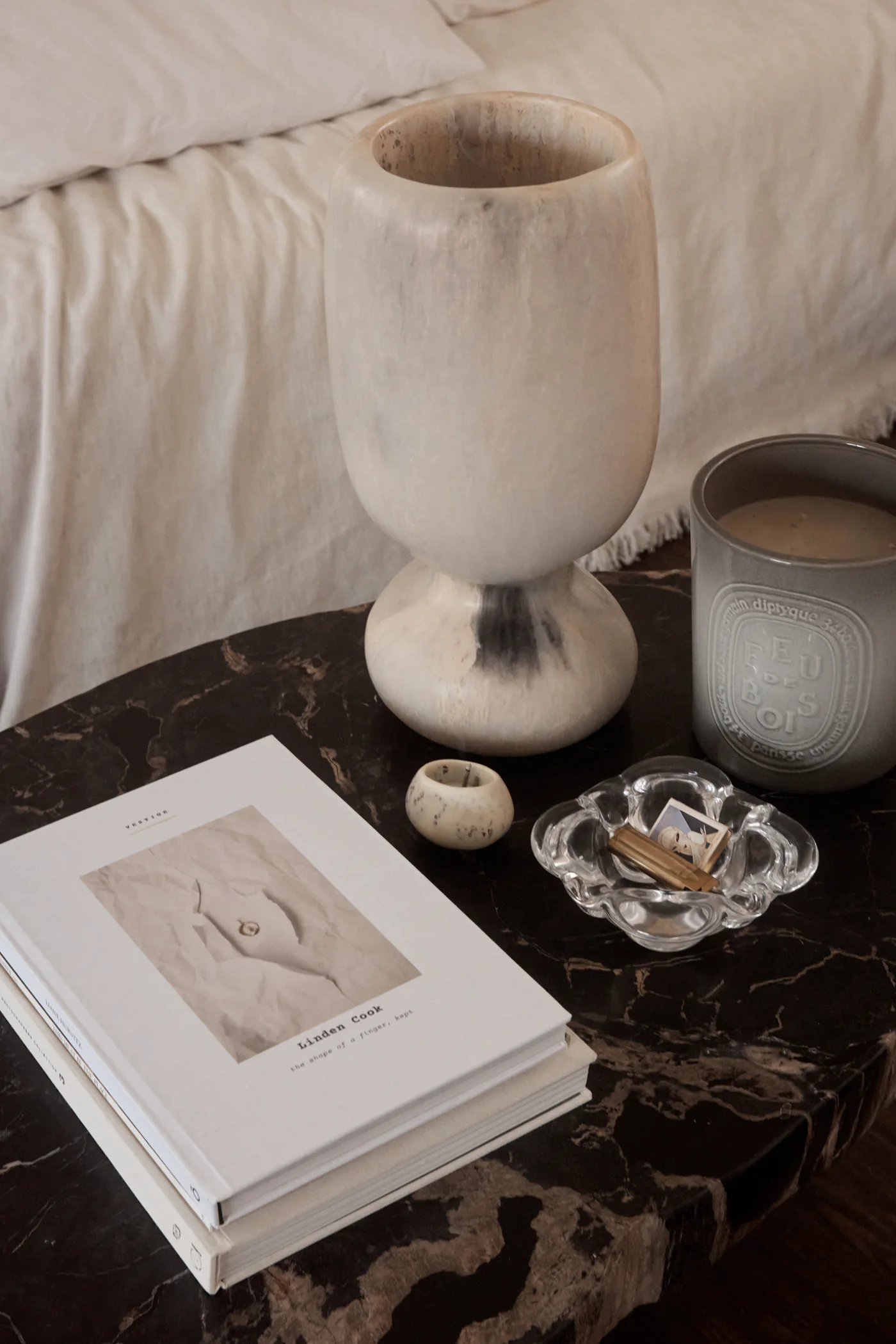 A Vestige hardcover book, Linden Cook — the shape of a finger, kept — on a dark marble table beside a stone vase and a candle