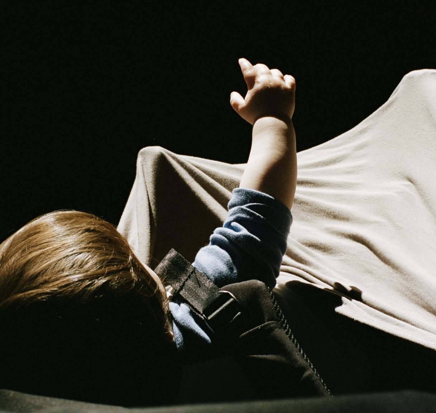 A small child lying in a shaft of hard sunlight, one hand raised into the light, everything around him in shadow